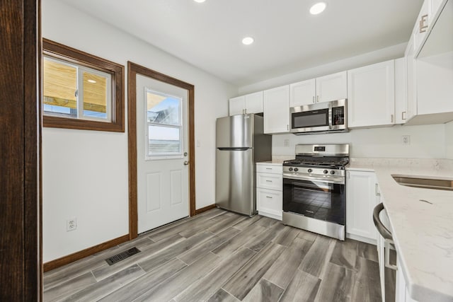 kitchen with stainless steel appliances, wood tiled floor, white cabinetry, light stone countertops, and baseboards