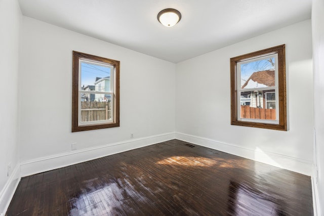 empty room with dark wood finished floors, visible vents, and baseboards