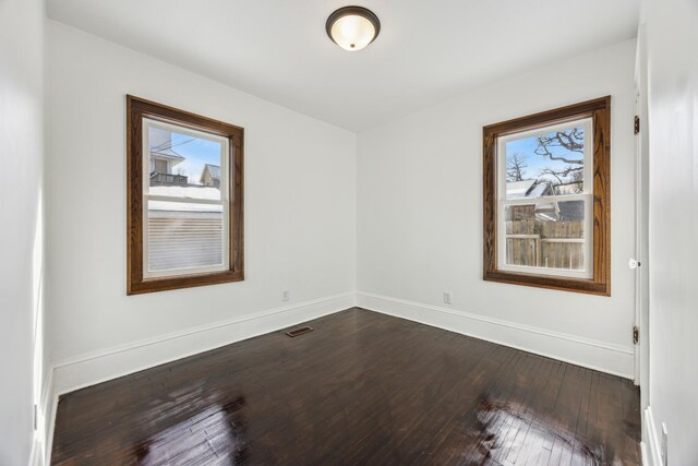 empty room featuring visible vents, baseboards, and dark wood-style flooring