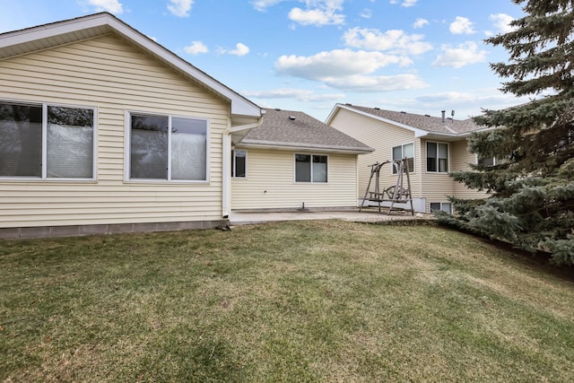 back of property featuring roof with shingles, a lawn, and a patio area