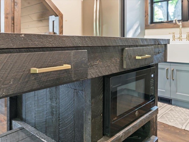 interior details with dark countertops, visible vents, a sink, wood finished floors, and stainless steel fridge