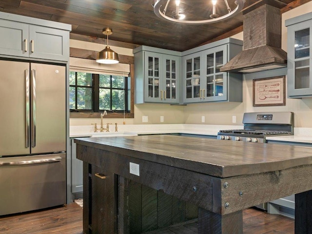 kitchen with butcher block counters, wall chimney exhaust hood, wood ceiling, appliances with stainless steel finishes, and a sink