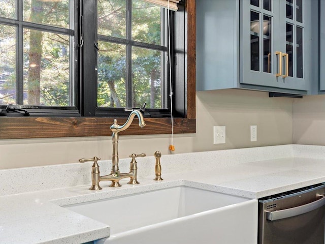 interior details featuring light stone counters, a sink, stainless steel dishwasher, gray cabinets, and glass insert cabinets