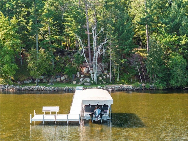 view of dock featuring a wooded view, a water view, and boat lift