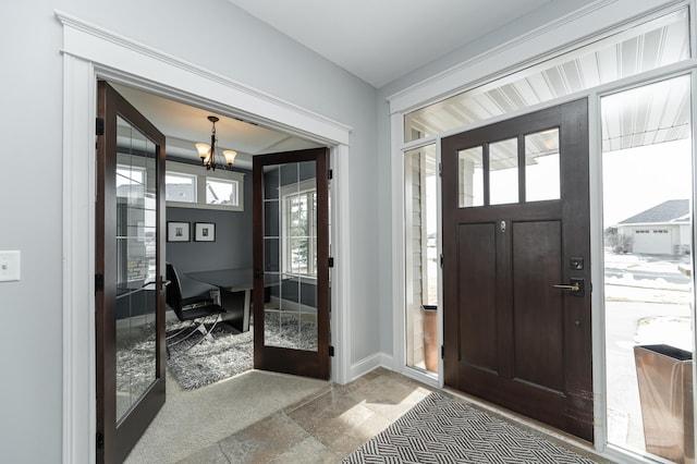 carpeted entrance foyer featuring a healthy amount of sunlight, french doors, baseboards, and an inviting chandelier