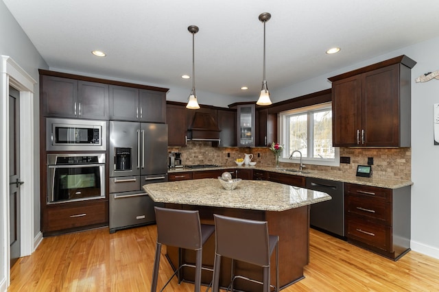 kitchen featuring dark brown cabinets, premium range hood, light wood-style floors, stainless steel appliances, and a sink