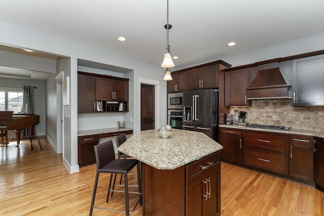 kitchen featuring tasteful backsplash, a kitchen island, premium range hood, appliances with stainless steel finishes, and light wood-style floors