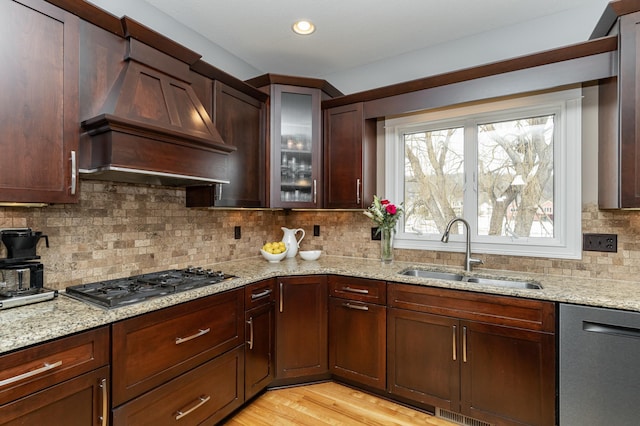 kitchen with light stone countertops, custom range hood, decorative backsplash, stainless steel appliances, and a sink