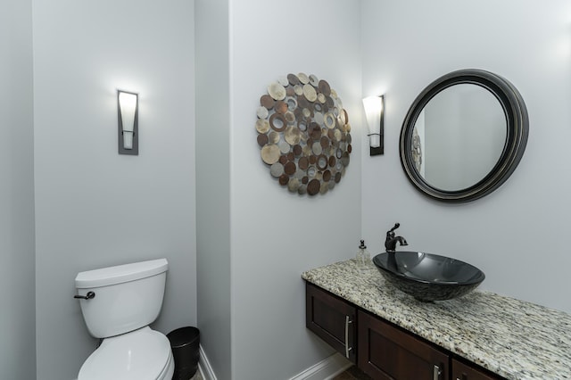 half bathroom with vanity, toilet, and baseboards