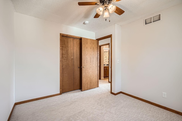 unfurnished bedroom featuring visible vents, a textured ceiling, a closet, baseboards, and light colored carpet