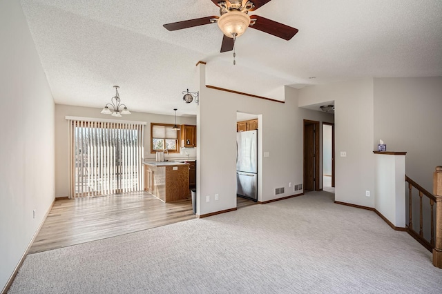 unfurnished living room featuring baseboards, lofted ceiling, light carpet, ceiling fan with notable chandelier, and a textured ceiling