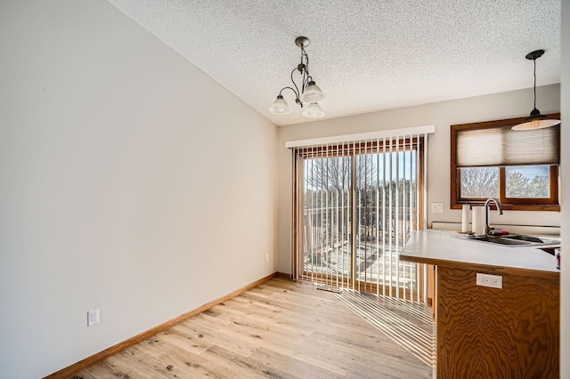 unfurnished dining area featuring light wood finished floors, a textured ceiling, baseboards, and a sink