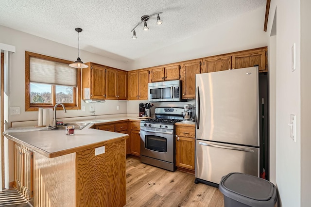 kitchen featuring a sink, appliances with stainless steel finishes, a peninsula, brown cabinetry, and vaulted ceiling