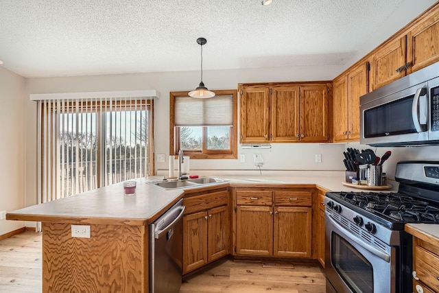 kitchen with light wood finished floors, appliances with stainless steel finishes, brown cabinetry, and a sink