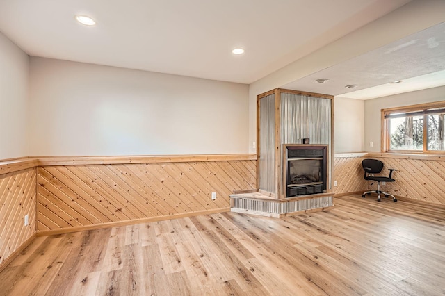 unfurnished living room featuring a fireplace, wood finished floors, wood walls, and wainscoting