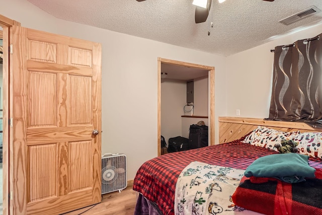 bedroom with ceiling fan, light wood-style floors, visible vents, and a textured ceiling