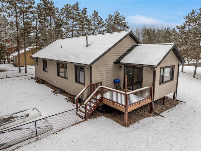 snow covered property with a shingled roof, a deck, and fence