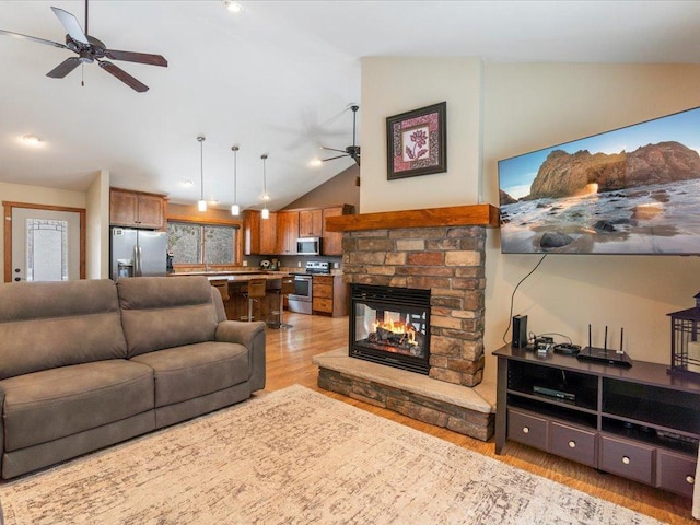 living area featuring a stone fireplace, lofted ceiling, light wood-type flooring, and ceiling fan