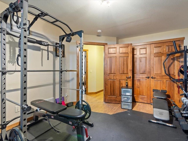 exercise room with light wood-style flooring, a textured ceiling, and baseboards