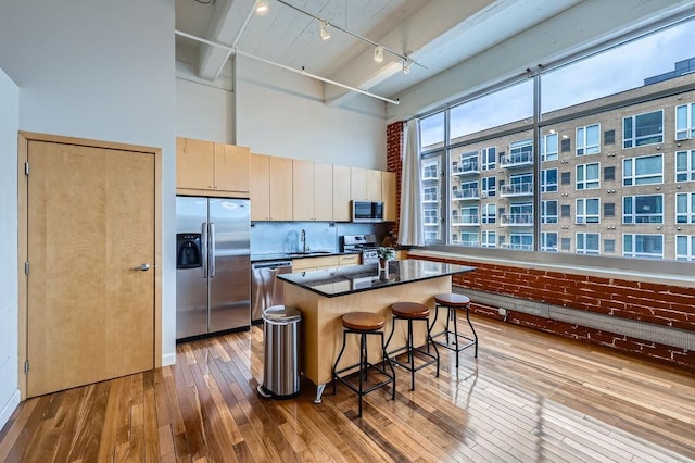 kitchen with hardwood / wood-style flooring, stainless steel appliances, a high ceiling, a sink, and a center island