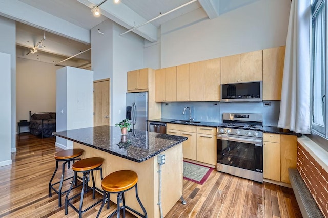 kitchen featuring light brown cabinets, a high ceiling, a sink, appliances with stainless steel finishes, and a kitchen bar