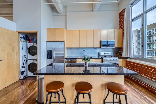 kitchen with a breakfast bar, stainless steel appliances, stacked washer / drying machine, a high ceiling, and a sink