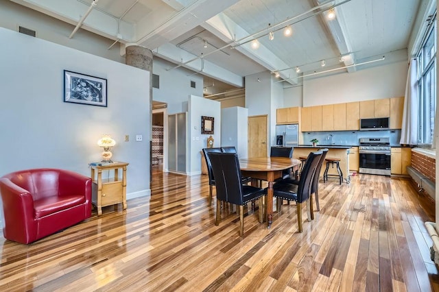 dining room featuring track lighting, light wood-type flooring, visible vents, and a high ceiling