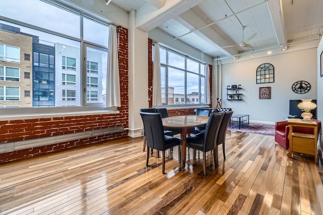 dining room featuring beam ceiling, brick wall, baseboards, and hardwood / wood-style floors