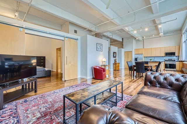 living room featuring a barn door, baseboards, a towering ceiling, rail lighting, and light wood-style floors