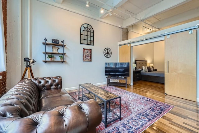 living room with rail lighting, a barn door, baseboards, and wood finished floors