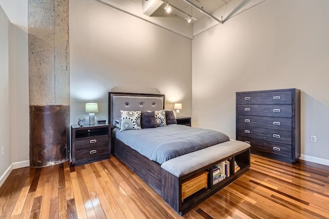 bedroom with rail lighting, baseboards, and hardwood / wood-style floors