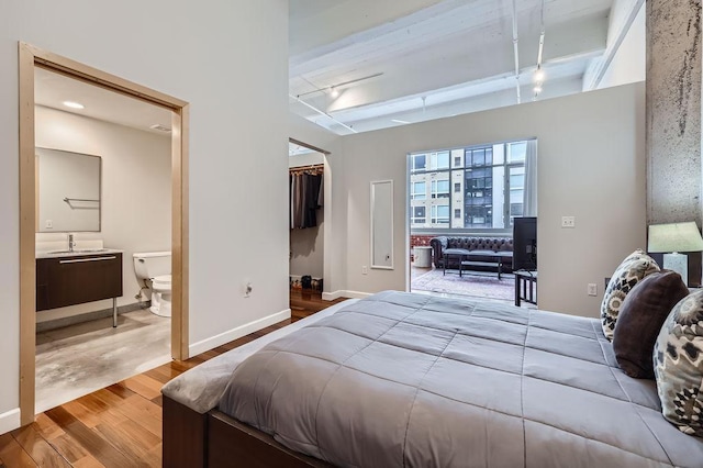 bedroom featuring a sink, wood finished floors, baseboards, a walk in closet, and track lighting