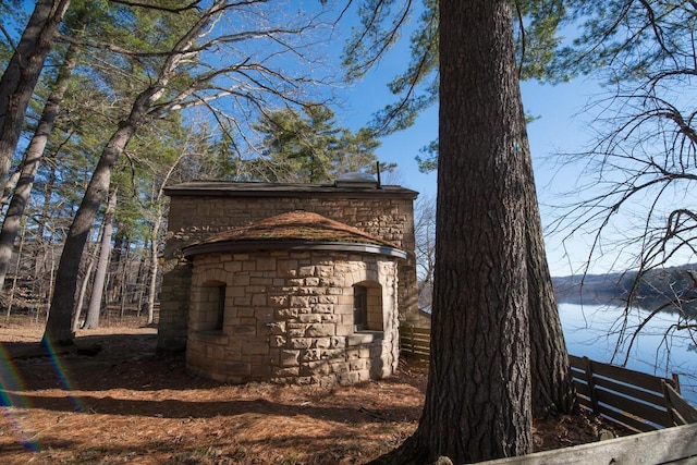 view of side of property featuring a water view, stone siding, and fence