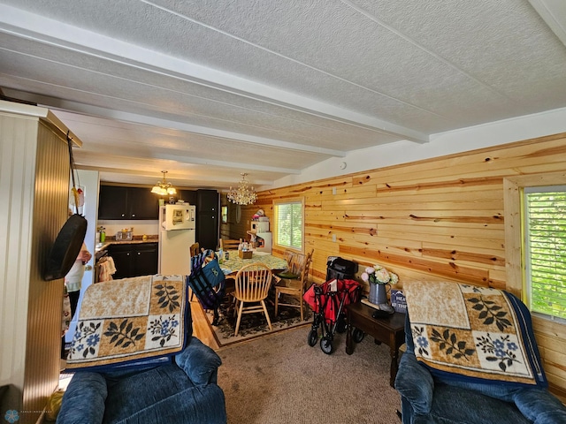 living room featuring a healthy amount of sunlight, carpet, wood walls, beam ceiling, and an inviting chandelier