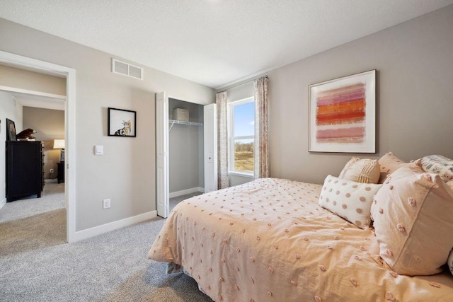 bedroom with baseboards, visible vents, light colored carpet, a textured ceiling, and a closet