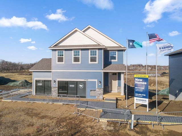 view of front of house with stone siding, fence, and roof with shingles