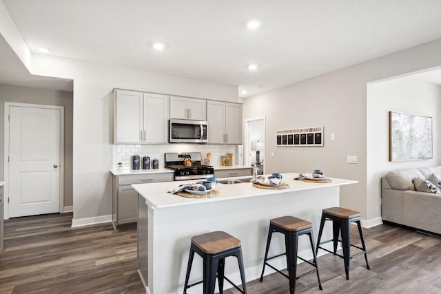 kitchen featuring dark wood-style floors, a breakfast bar, stainless steel appliances, tasteful backsplash, and light countertops