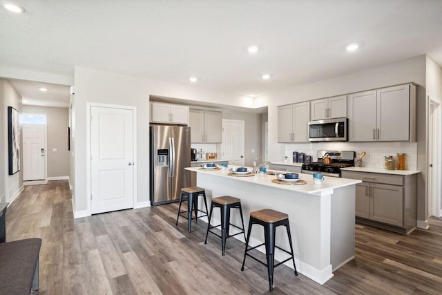 kitchen featuring stainless steel appliances, gray cabinets, dark wood-type flooring, an island with sink, and a kitchen breakfast bar