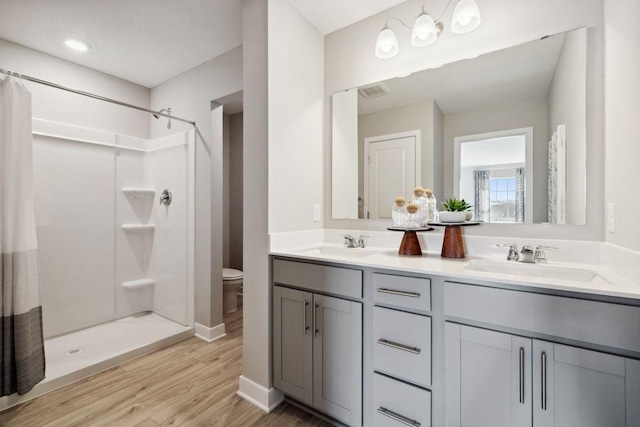 full bathroom featuring double vanity, wood finished floors, a sink, and a shower stall