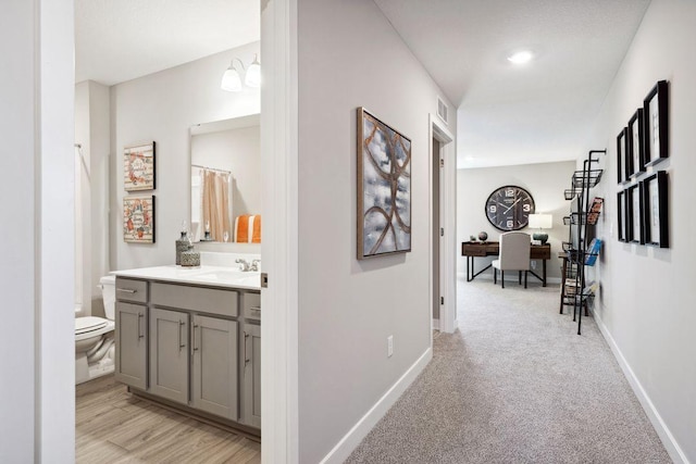 hallway featuring visible vents, a sink, light colored carpet, and baseboards