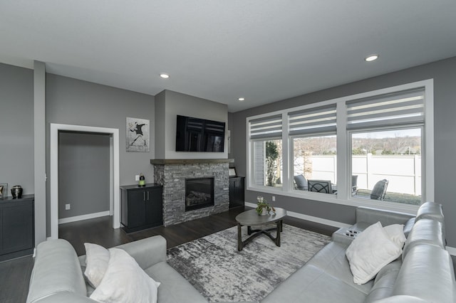 living area with a wealth of natural light, dark wood finished floors, a stone fireplace, and baseboards