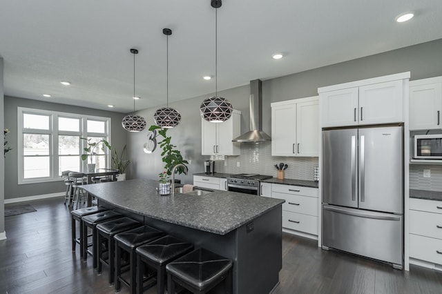 kitchen with stainless steel appliances, decorative backsplash, a sink, wall chimney range hood, and a kitchen bar