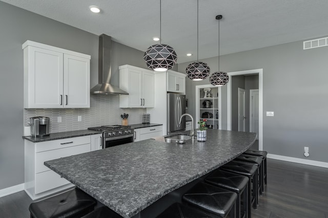 kitchen with dark countertops, wall chimney range hood, stainless steel appliances, and a sink