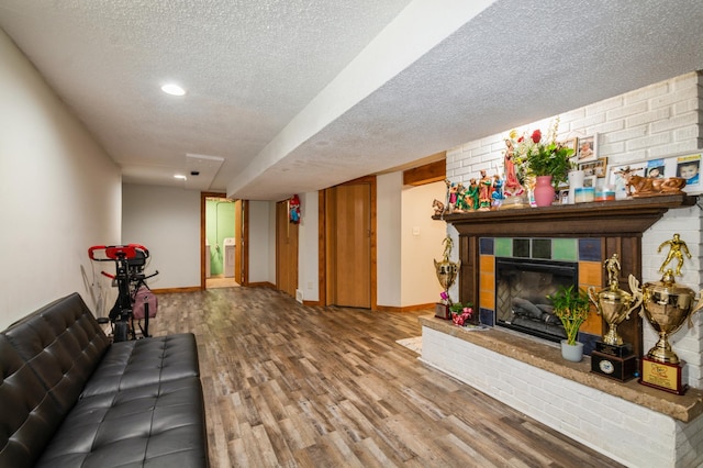 living room with a textured ceiling, baseboards, wood finished floors, and a tiled fireplace