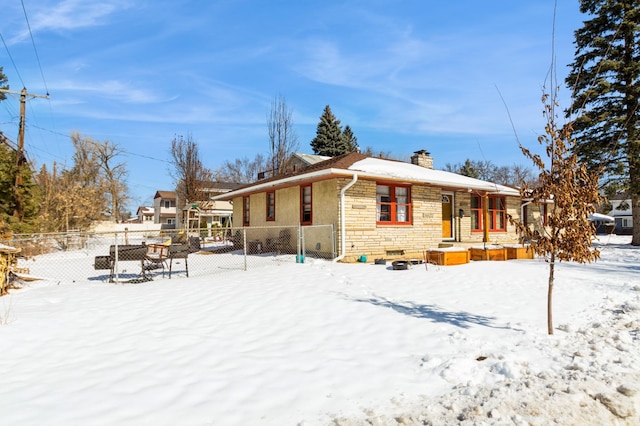 view of snow covered exterior with stone siding, a chimney, and fence