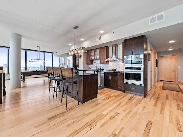 kitchen featuring wall chimney range hood, a breakfast bar area, visible vents, and appliances with stainless steel finishes