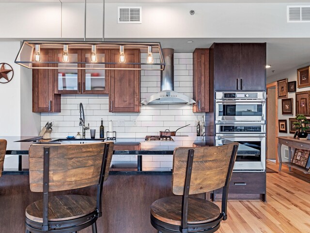 kitchen featuring a kitchen bar, wall chimney exhaust hood, visible vents, and stainless steel double oven