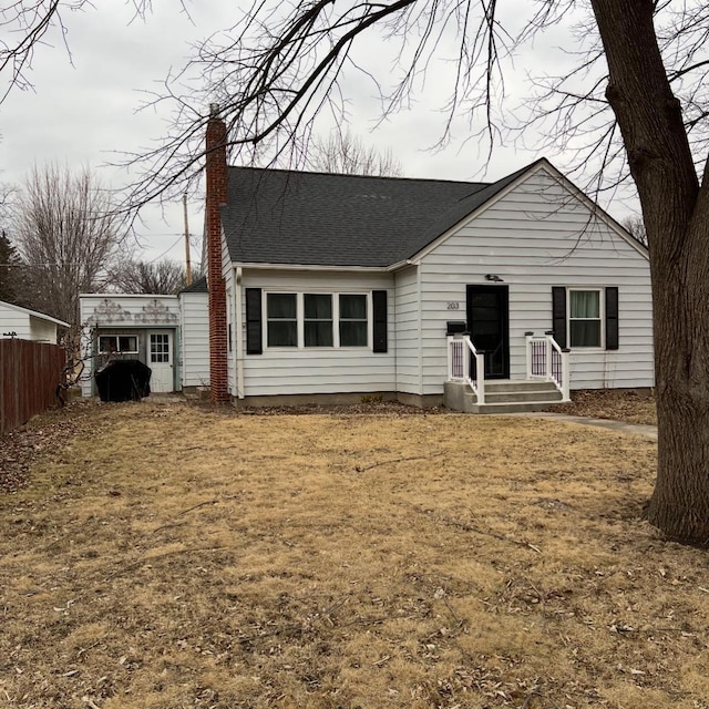 view of front of property featuring roof with shingles, fence, and a chimney