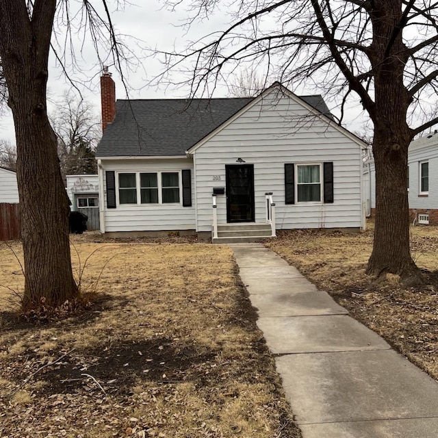 view of front of home featuring a shingled roof, fence, and a chimney