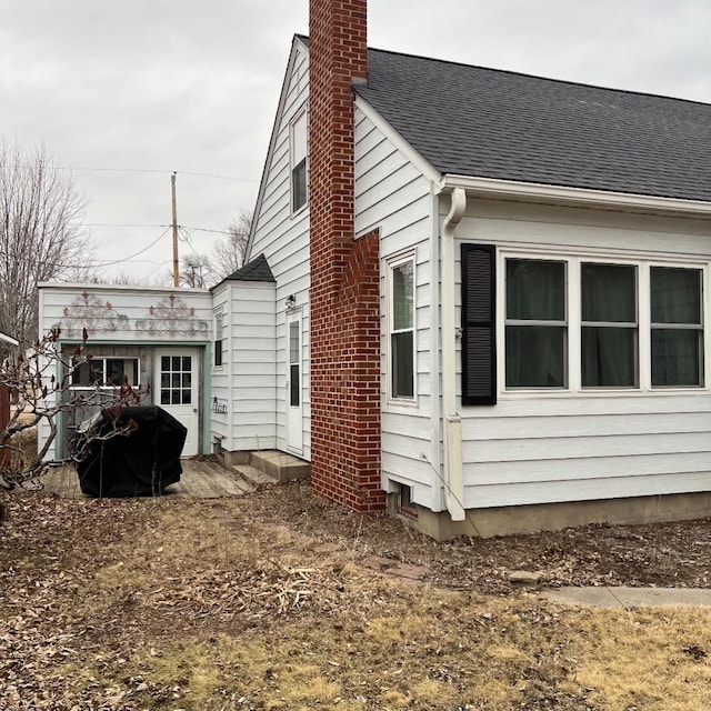 view of home's exterior with roof with shingles and a chimney